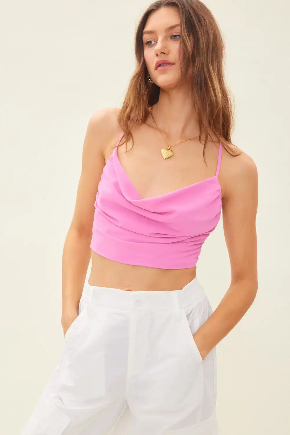 A woman wearing a pink cowl neck crop top and white wide-leg pants.